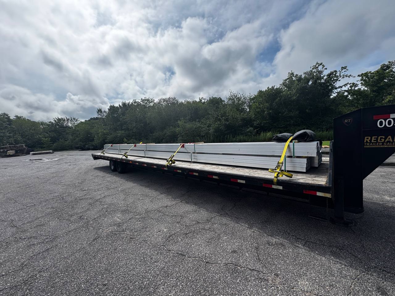 Long aluminum tubing secured with straps on a flatbed trailer.
