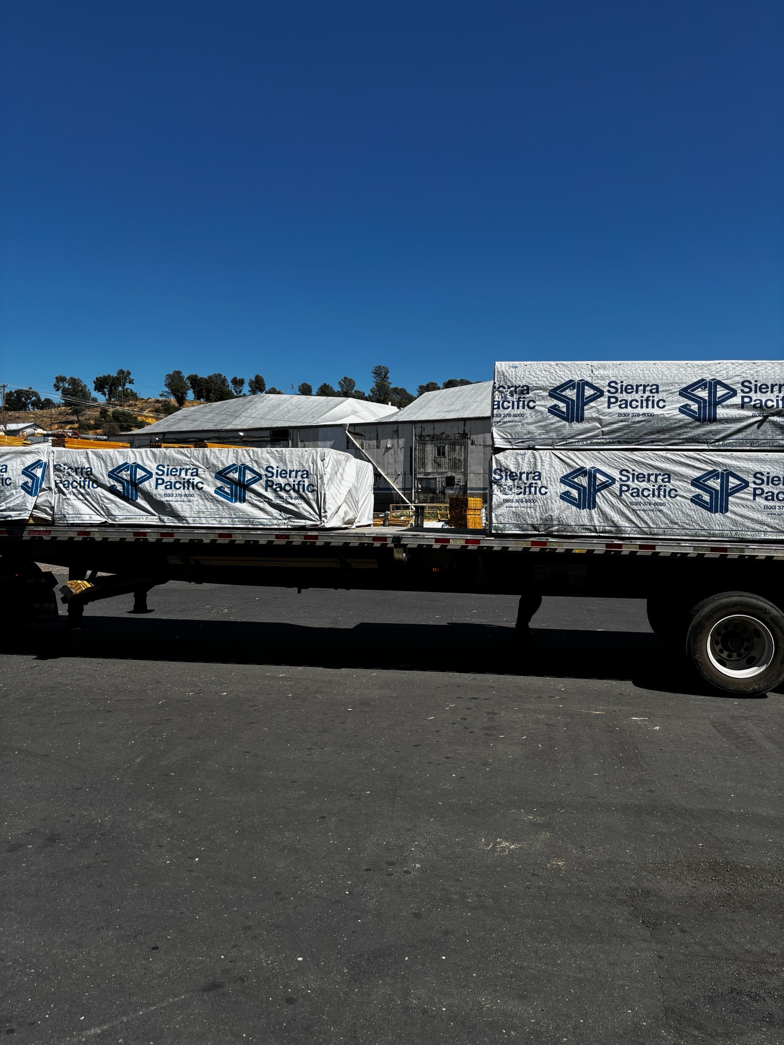Sierra Pacific lumber delivery on flatbed truck with branded tarps covering wood products at a California distribution yard.