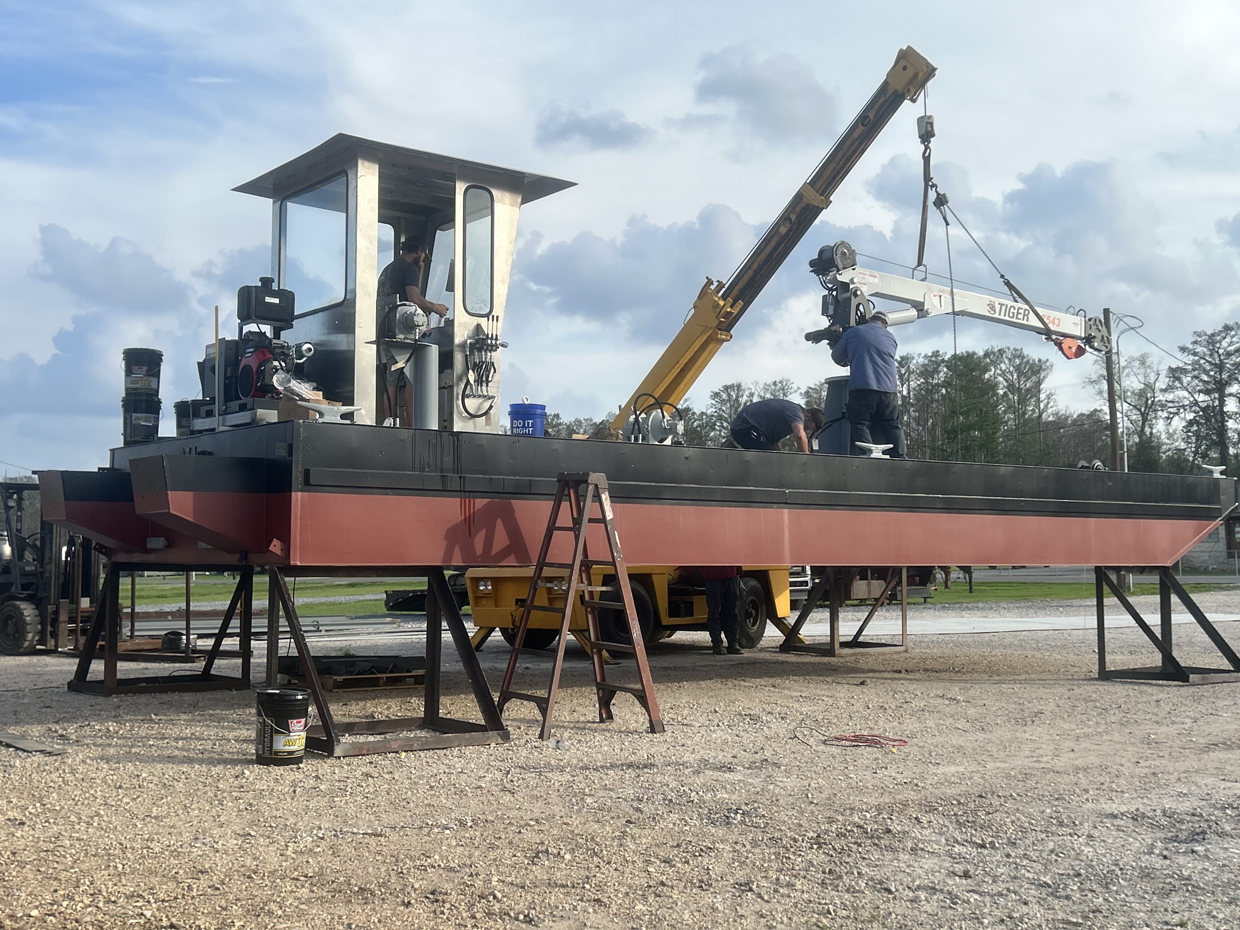 Assembling a steel work barge hull on support stands with a Tiger crane and operator cab at the fabrication yard. Getting ready to ship!