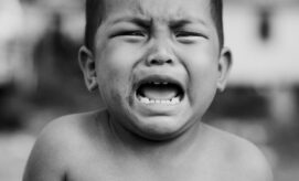 A young child is crying loudly, mouth open, tears streaming down, amidst an out-of-focus, blurred outdoor setting.