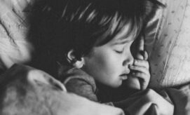 A child peacefully sleeps, resting their head on a pillow, with hand tucked under their chin, in a cozy and dimly lit bedroom environment.