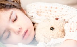 Child sleeping peacefully, cuddling a plush teddy bear under a knitted blanket, creating a serene and cozy atmosphere.