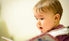 A young child attentively looks at a book, captivated by its contents, in a softly lit indoor setting.
