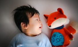 A baby lies on a soft surface gazing at a plush toy fox, creating a calm and playful interaction in a cozy indoor setting.