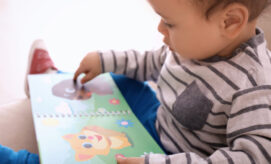 A child, wearing a striped shirt, sits and focuses on touching colorful illustrations in a book with animal images, in a cozy indoor setting.