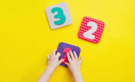 Children's hands assemble textured number blocks, "1," "2," and "3," against a bright yellow background.