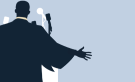 A silhouetted figure gestures with an outstretched arm towards multiple microphones, set against a light background, suggesting a speaking engagement or public address.
