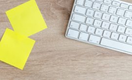 A white keyboard partially seen on a wooden desk; two blank yellow sticky notes are nearby, suggesting a workspace environment.