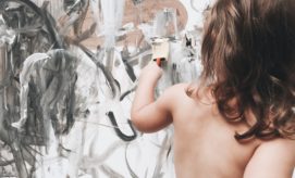 A child uses a paintbrush to create abstract art on a large canvas, featuring black and gray swirling patterns, in a creative and expressive setting.
