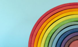Colorful wooden rainbow arcs arranged in a layered sequence from red to violet, occupying the right half of the image against a plain light blue background.