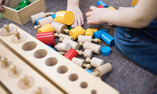 Montessori Curriculum style learning materials scattered on an early learning classroom floor with little hands at play