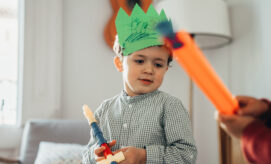 Two young boys enjoying pretend play in an early learning classroom–one wearing a homemade paper crown that he decorated.