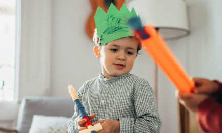 Two young boys enjoying pretend play in an early learning classroom–one wearing a homemade paper crown that he decorated.