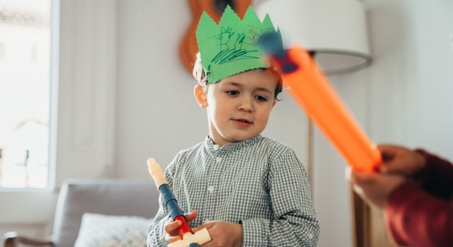Two young boys enjoying pretend play in an early learning classroom–one wearing a homemade paper crown that he decorated.