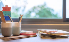 Preschool materials with pencils, children’s books, and colorful blocks organized neatly in front of a sunny window.