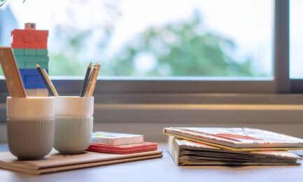 Preschool materials with pencils, children’s books, and colorful blocks organized neatly in front of a sunny window.