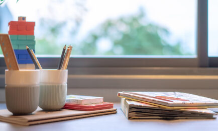 Preschool materials with pencils, children’s books, and colorful blocks organized neatly in front of a sunny window.