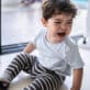 Toddler boy with curly hair, sitting on floor crying while caregiver stands beside him to assist and provide comfort.