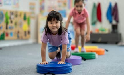 Two preschool-aged girls crawling over an indoor obstacle course to build motor skills through play.