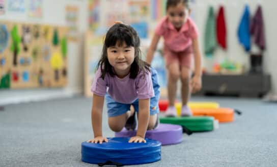 Two preschool-aged girls crawling over an indoor obstacle course to build motor skills through play.