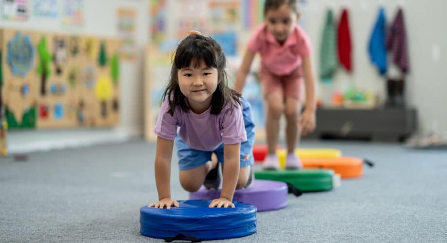 Two preschool-aged girls crawling over an indoor obstacle course to build motor skills through play.