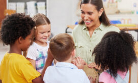 Group of preschool children, smiling, as they join around their educator and join her in playing a musical instrument.