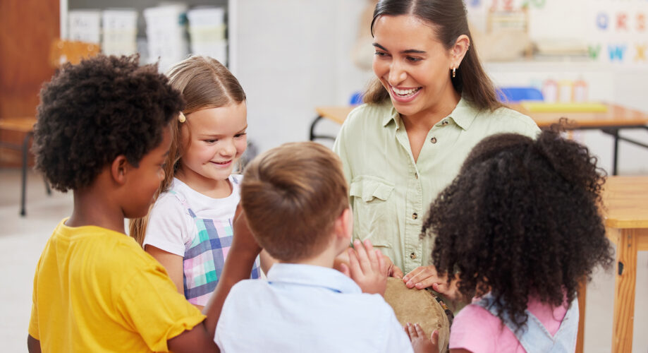 Group of preschool children, smiling, as they join around their educator and join her in playing a musical instrument.
