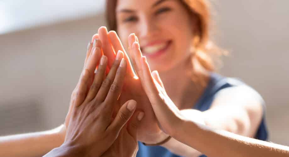 Group of women high five, while smiling and working together as a team.