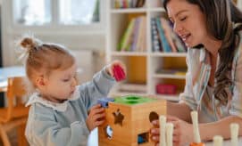 Educator in early learning classroom sitting at a table with a young girl as the two explore shapes and colors.