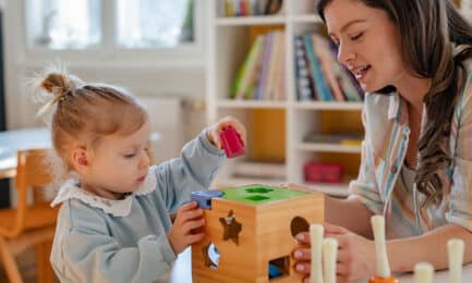 Educator in early learning classroom sitting at a table with a young girl as the two explore shapes and colors.
