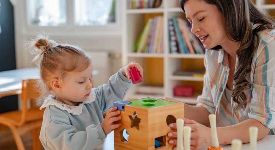 Educator in early learning classroom sitting at a table with a young girl as the two explore shapes and colors.