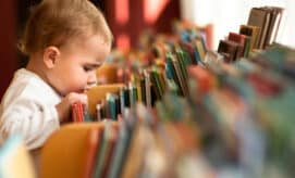 Toddler child peering into a display of children’s books, searching for a story to read.