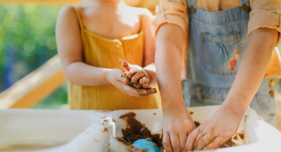 IMAGE ALT TEXT: Two young children enjoying sensory play outdoors, mixing water and sand in a large tub.