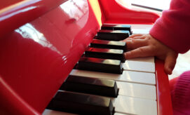 A young child’s hand plays keys on a mini piano in an early learning classroom.