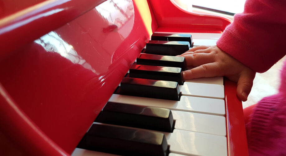 A young child’s hand plays keys on a mini piano in an early learning classroom.