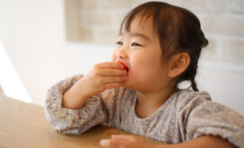 A young girl wearing pink overalls uses a paintbrush to paint with watercolors on a large block of ice.