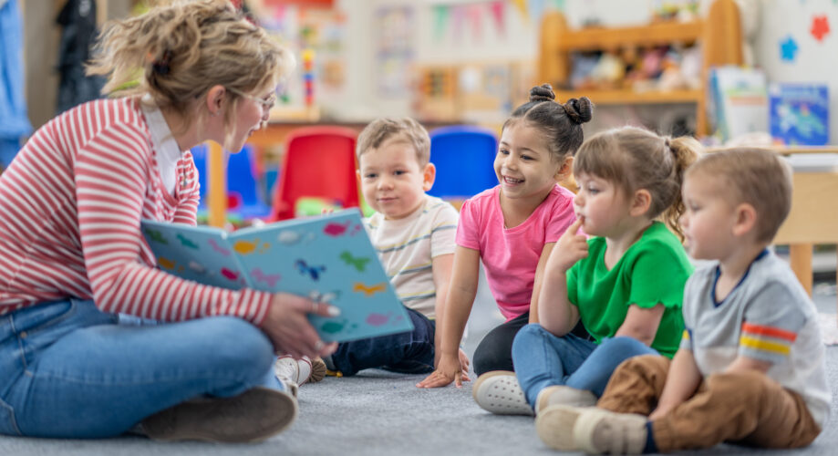 A teacher reads a picture book to a group of young children during circle time in an early learning classroom.