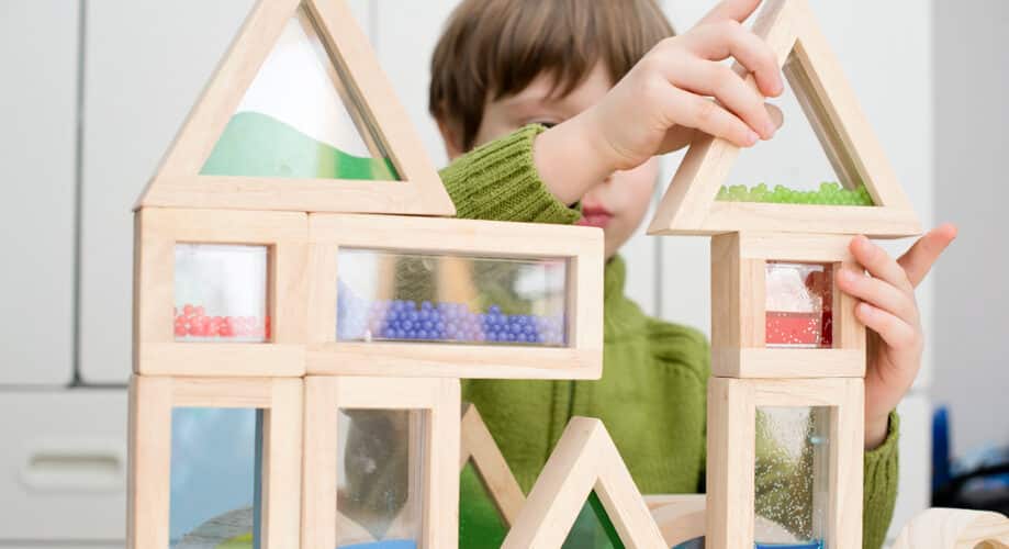 Young boy stacks colorful blocks together, exploring STEM concepts in an early learning classroom.
