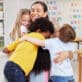 A group of preschool children hug their teacher in an early childhood education classroom.