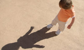 Toddler child plays outdoors and explores his shadow on a summer day.