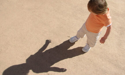 Toddler child plays outdoors and explores his shadow on a summer day.