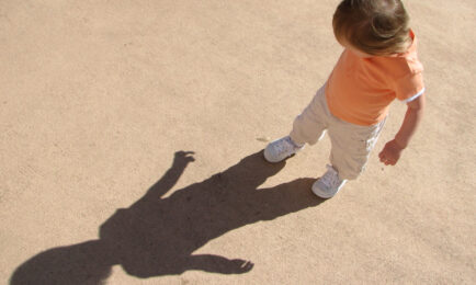 Toddler child plays outdoors and explores his shadow on a summer day.
