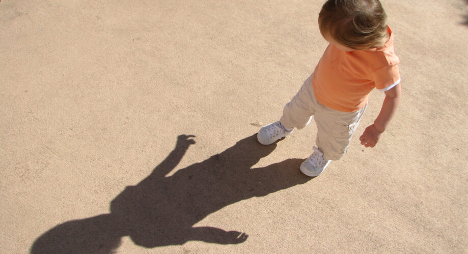 Toddler child plays outdoors and explores his shadow on a summer day.