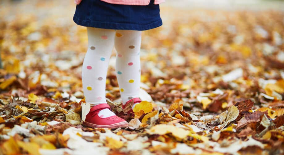 Toddler child walks through Autumn leaves.