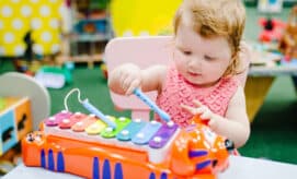 Toddler girl plays with xylophone, making music in an early learning classroom.