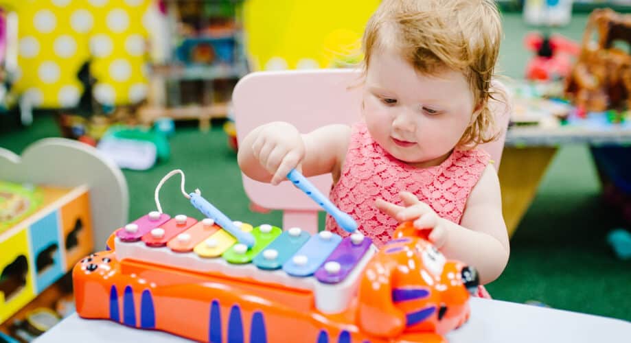 Toddler girl plays with xylophone, making music in an early learning classroom.