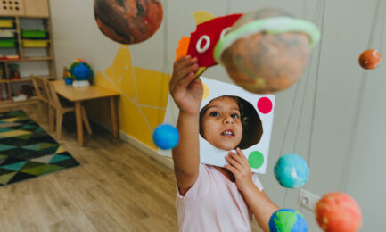Preschool girl plays with a hanging solar system display in her early learning classroom.