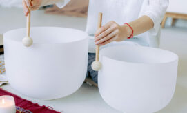 A person sits on the ground and plays crystal bowls in a calming meditation experience.