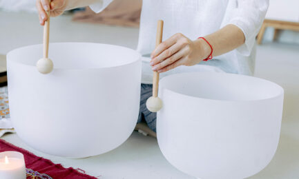 A person sits on the ground and plays crystal bowls in a calming meditation experience.