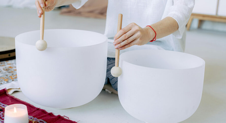 A person sits on the ground and plays crystal bowls in a calming meditation experience.